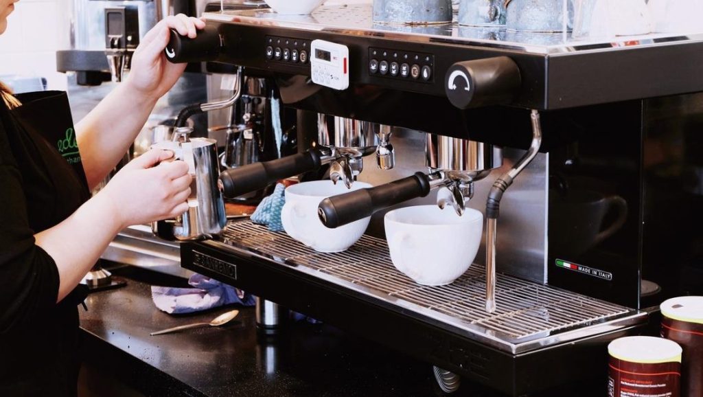 Barista onderhoudt professionele koffiemachine met dagelijks schoonmaken en reinigen van zetgroep